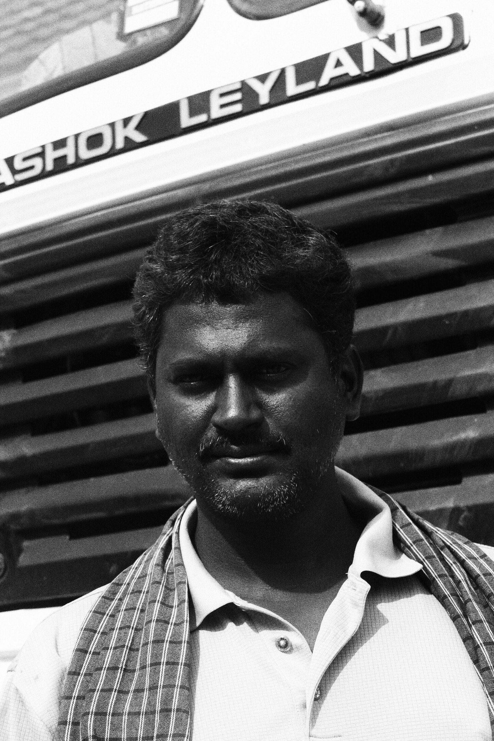 Monochrome portrait of a man standing in front of Ashok Leyland truck.